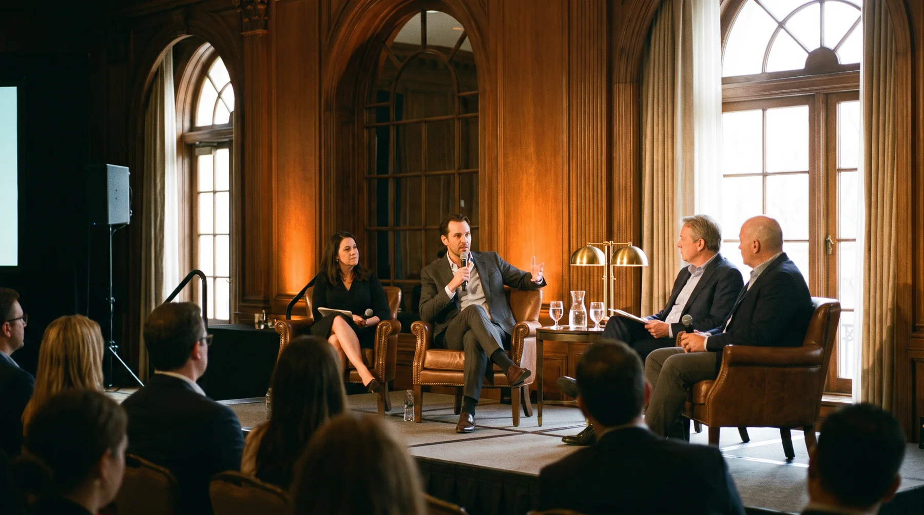 A business broker mid-sentence on a panel at an industry conference, explaining an idea to a seated audience